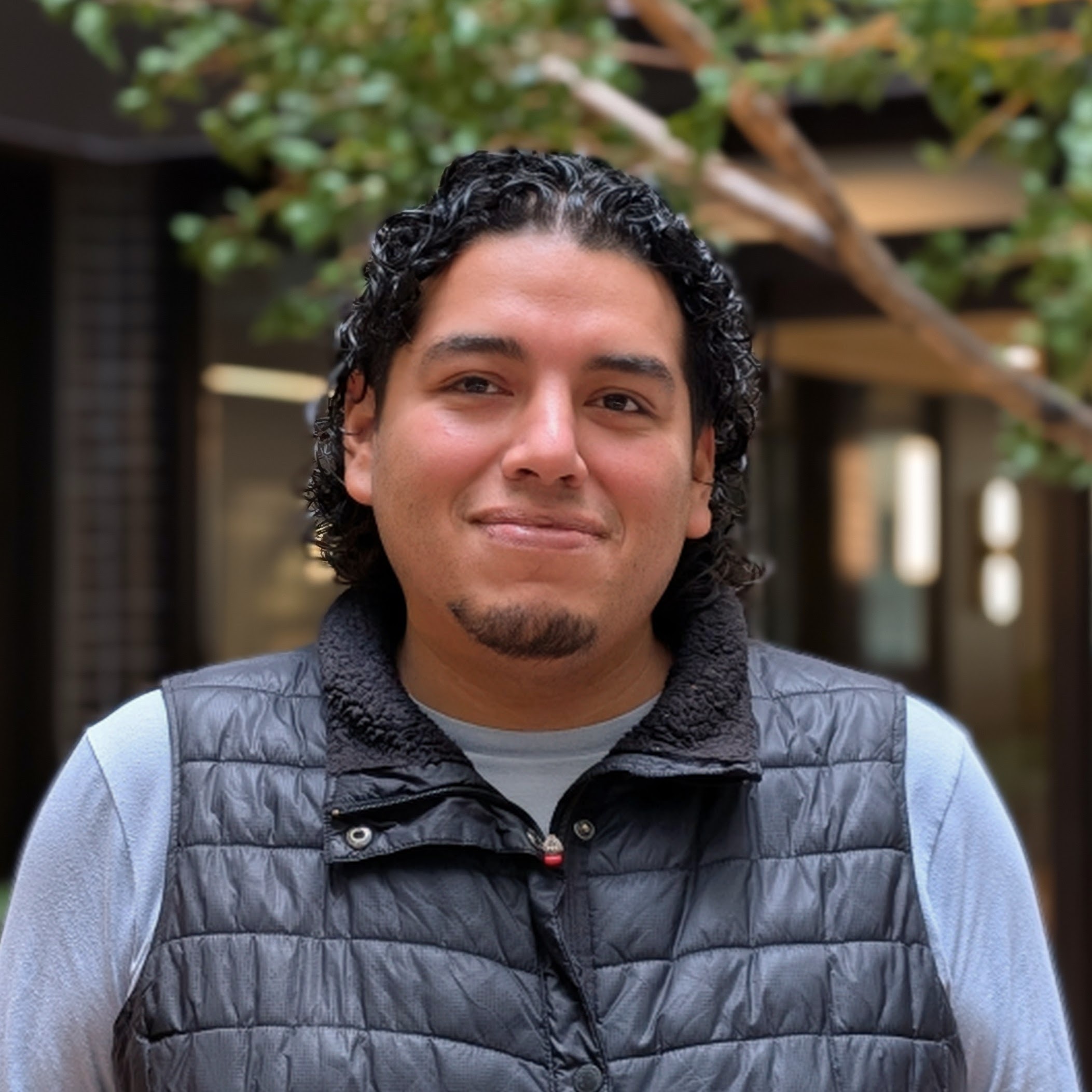 J'orge Garcia J'orge Garcia is pictured from the shoulders up, wearing a blue shirt and black vest with black curly hair