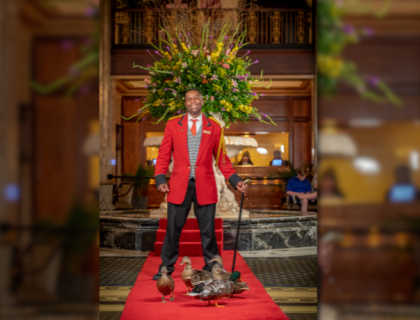 Kenon Walker stands on a red carpet with five ducks at his feet 