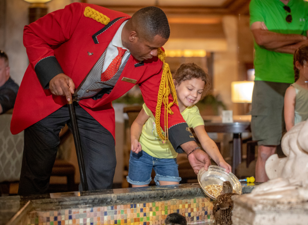 Duckmaster Kenon and a child feed a duck in the hotel lobby's fountain