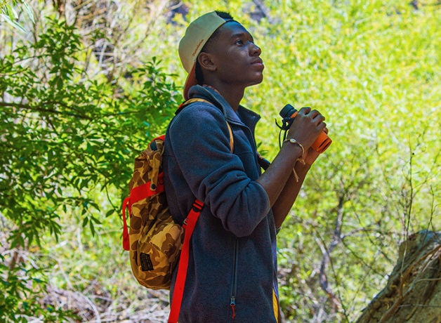 A photo of Isaiah Scott birding with binoculars in lush green habitat.