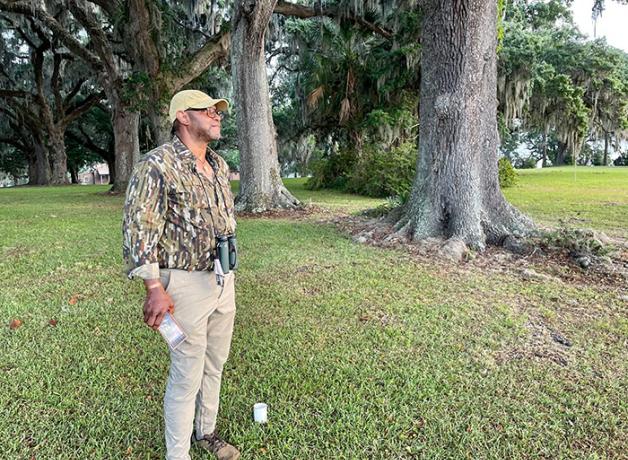 Professor Drew Lanham stands beneath large trees on bank of a former rice plantation in Virginia.