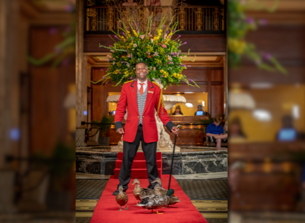 Kenon Walker stands on a red carpet with five ducks at his feet 