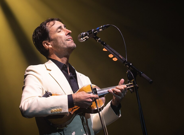 Man stands singing at microphone, strumming a violin