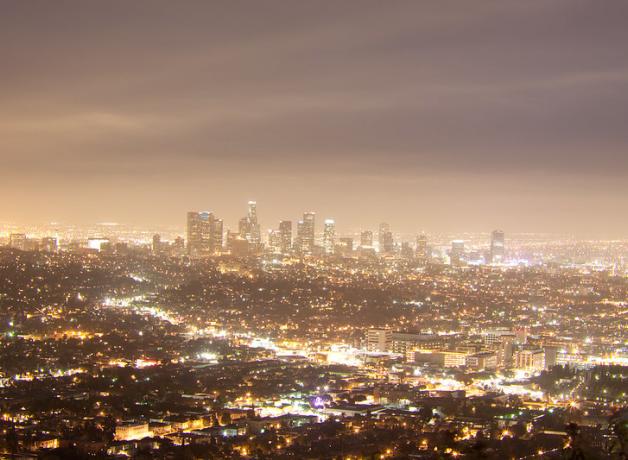 A night scene of Los Angeles seen from a nearby hill. The dense city lights make a milky glow in the sky above.