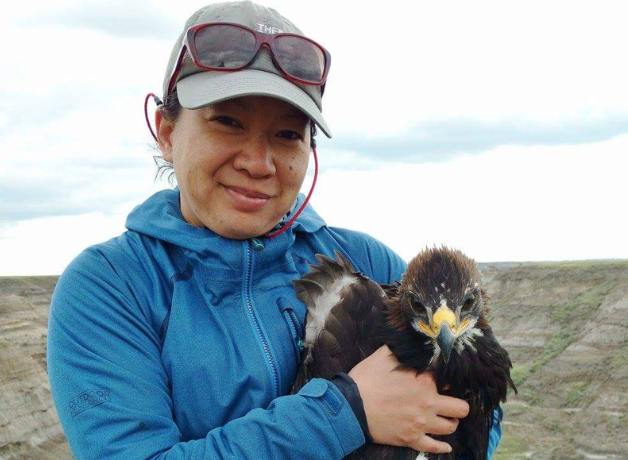 Janet Ng, wearing gray baseball cap and blue jacket, holds an immature Golden Eagle in her arms