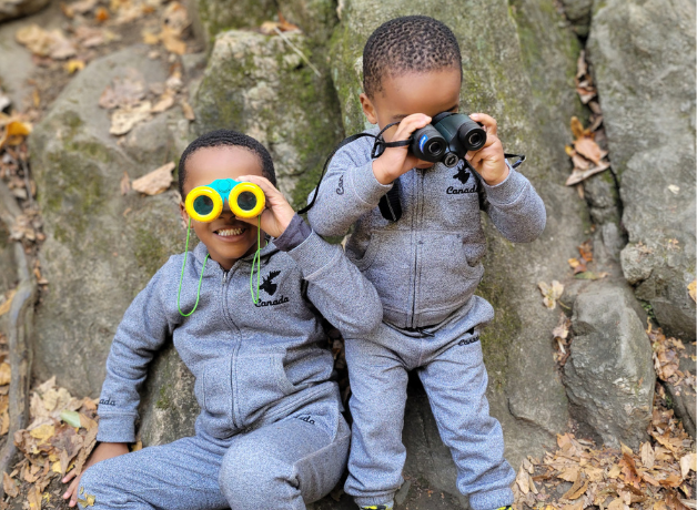 Two little boys in matching outfits holding binoculars outside.