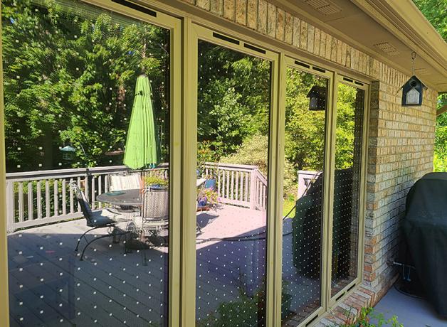 Windows reflecting an outside deck and backyard; the windows have Feather Friendly dots on them to prevent bird crashes
