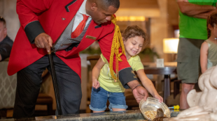 Duckmaster Kenon and a child feed a duck in the hotel lobby's fountain