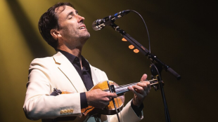 Man stands singing at microphone, strumming a violin