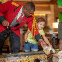 Duckmaster Kenon and a child feed a duck in the hotel lobby's fountain